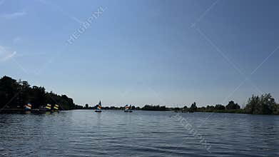 Small sailboats crossing calm river under clear summer sky, framed by green