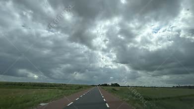 Empty rural road stretching through flat green fields beneath dramatic storm