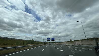 Busy motorway with cars under dramatic cloudy sky, direction signs ahead
