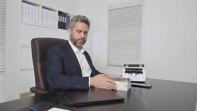 Businessman working on laptop with stacks of money in office. Business concept with cash and digital work. Banker in office