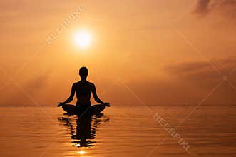Woman practicing yoga, silhouette on the beach at sunset