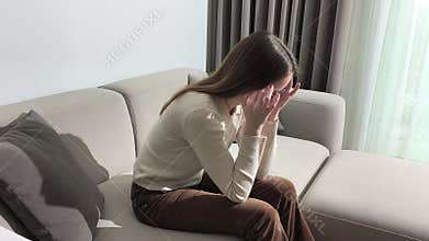 Woman sits on sofa leaning forward massaging temples. Female lowers