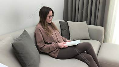 Woman flips book pages then closes it and leaves sofa
