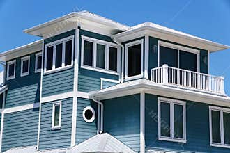 A modern coastal home with blue-green siding, white trim, large windows, and a metal roof in Anna Maria Island, Florida
