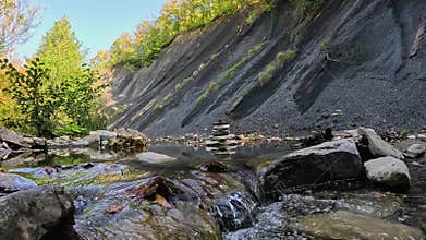 Balanced stone cairn on riverbank amid rushing mountain stream. Boulders, trekking, alpine climbing, hiking, backpacking and