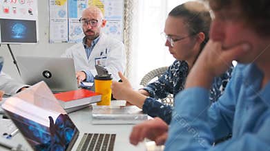 Bald doctor holding report while colleagues write notes and use laptops