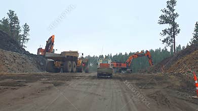 United States April 2 2026, Road construction convoy follows a pilot car between excavators and dump trucks in a
