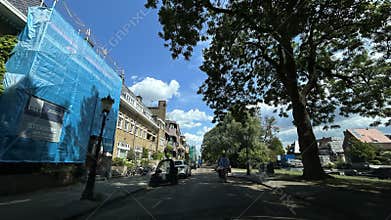 Quiet residential street with blue construction covering on brick house, leafy