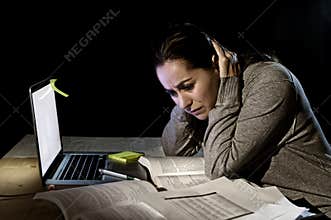 Young desperate university student girl in stress for exam studying with books and computer laptop late at night