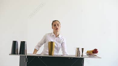 Professional bartender girl juggling bottles and shaking cocktail at mobile bar table on white background studio indoors
