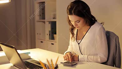 Woman with calculator and papers at night office