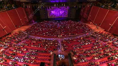 Spectators gather in the auditorium and watch the show in theatre timelapse. Large hall with red armchairs seats