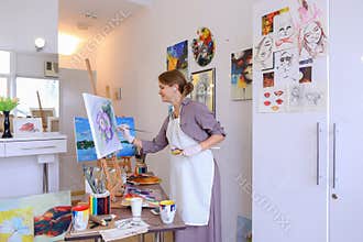 Beautiful young painter paints picture uses brushes and oil, and