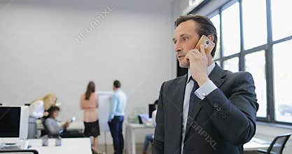 Businessman making decisions during phone call in modern office while group of business people team on meeting