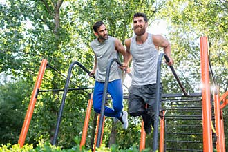 Two handsome young men passionate about fitness doing dips exerc