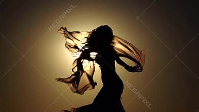 Girl with a veil in her hands dancing belly dance on the beach. Silhouette. Slow motion