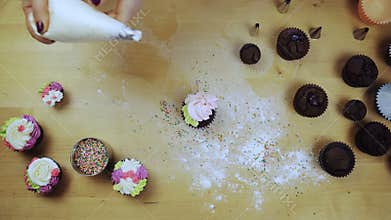 Top view of female hands decorating the chocolate cupcakes. Young woman using the pastry bag for colored cream.