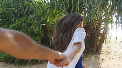 Girl holding male hand and running on tropical exotic beach to the ocean. Follow me shot of young woman pull her