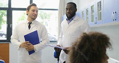 Two scientists shake hands walking in modern laboratory looking at female reseachers making experiment analysis in lab
