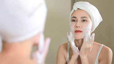 Woman cleaning washing her face with foam in bathroom.
