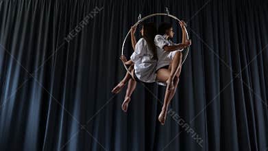 Charming gymnasts sits and spins in the aerial hoop