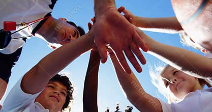 School kids and coach stacking hands in campus