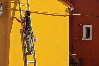 Close-up of painter painting wall of house of yellow in Burano.