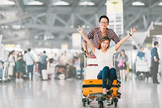 Asian tourist couple happy and excited together for the trip, girlfriend sitting and cheering on baggage trolley or luggage cart