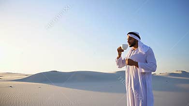 Good morning for male sheikh in middle of huge desert over cup of coffee against blue sky and dunes in open air.