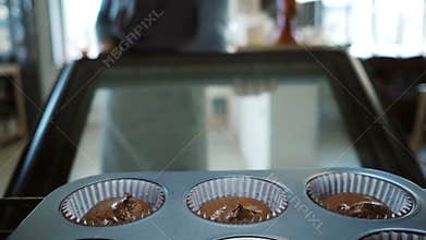 View inside: young woman open oven and putting in baking tray for cupcakes. Female dancing while waiting the desserts.