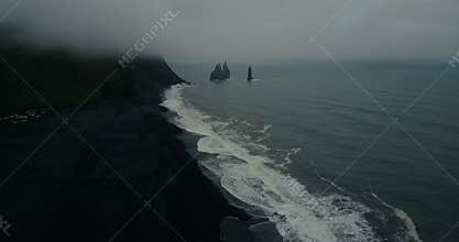 Aerial view of the black volcanic beach in Iceland and troll toes rocks in the sea. Copter flying over wave with foam.