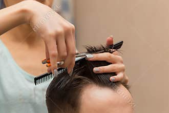 close up of hands of young barber making haircut to attractive man in barbershop