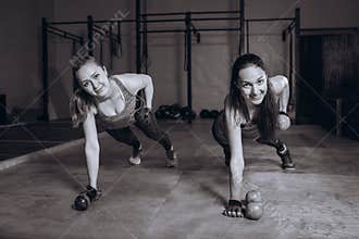 Two fit women in gym doing fitness exercises with dumbbells staying in plank pose, black and white