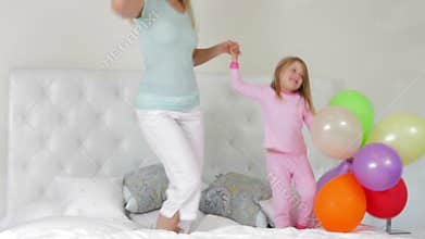 Mother And Daughter Jumping On Bed Holding Balloons