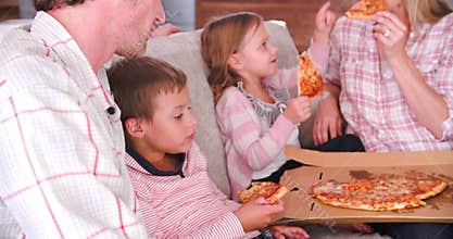 Family Sitting On Sofa Eating Takeaway Pizza Together
