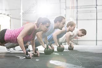 Side view of determined people doing pushups with kettlebells at crossfit gym