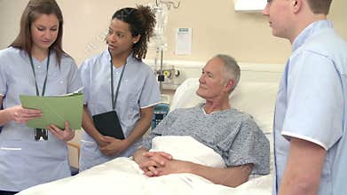 Medical Staff On Rounds Standing By Female Patient's Bed