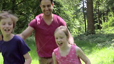 Father Chasing Children Along Woodland Path