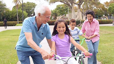 Grandparents Teaching Grandchildren To Ride Bikes In Park