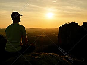 Man with baseball cap on top of mountain. Silhouette of rocks.