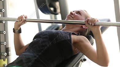 Young attractive lady working out in the gym - lifting barbell - chest muscles exercise