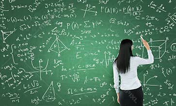 Rear view of a thoughtful woman who is writing math calculations on green chalk board.