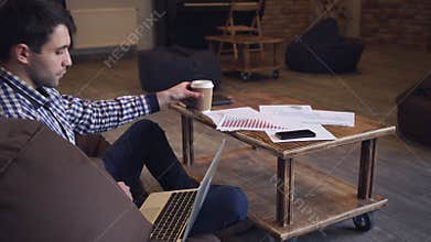 The man sitting resting, looking at the monitor and drinking coffee.