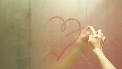 Hand draws a heart on a foggy mirror