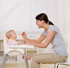 Mother feeding baby in highchair in kitchen