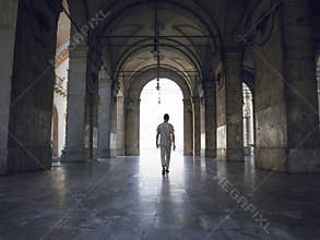 Man walking under heavy vaults, in Pisa, Italy. Bright light seeping in.