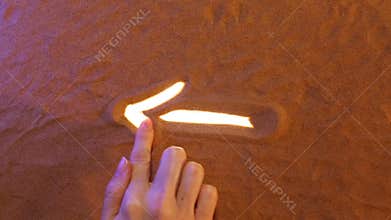 Hand drawing Arrow symbol in the sand. Beach background. Top view