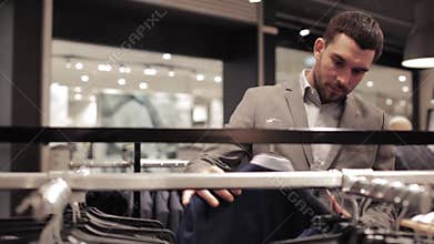 Young man choosing suit in clothing store or mall