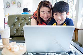 Asian Mother And Son Sitting At Desk Using Laptop At Home