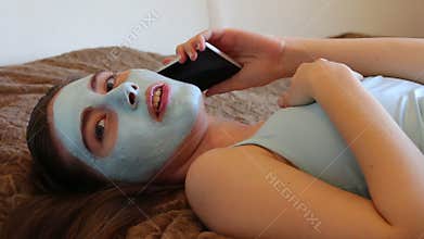 Girl with cosmetic mask on her face talking on the smartphone